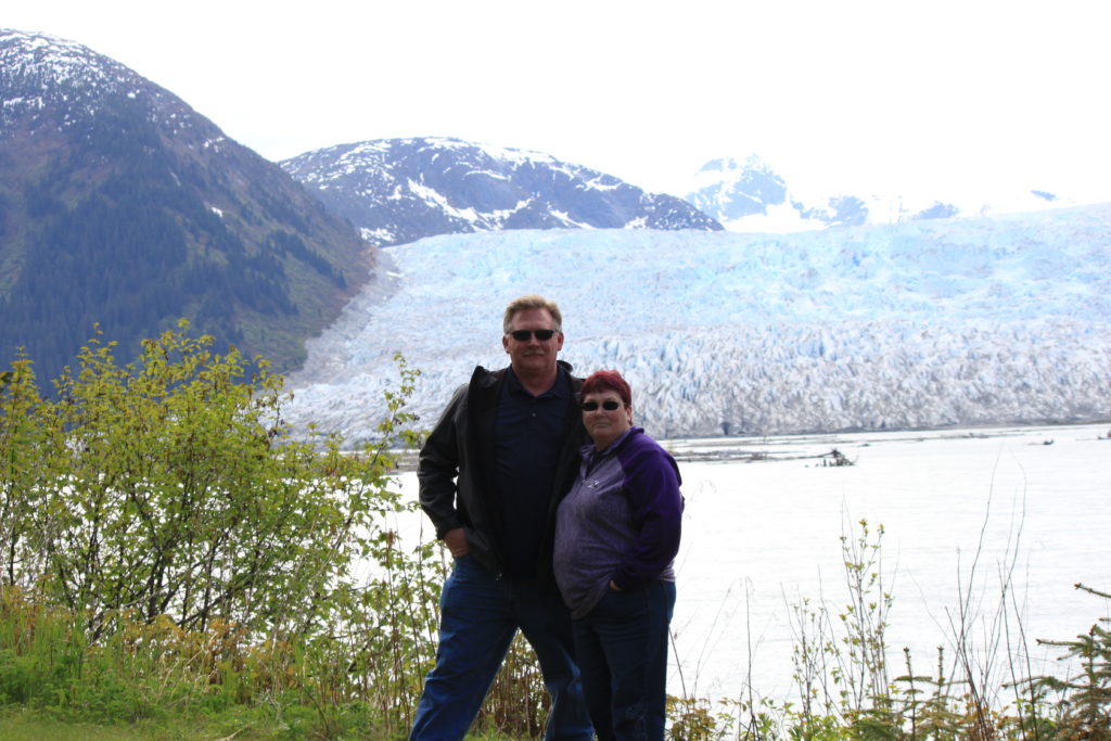 Man and woman standing in front of a lake with mountains beyond